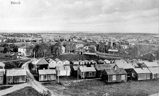 1918 Råneå vy söder.jpg - Bilden är tagen 1918, vägen som går mellan kyrkstugorna löper in mot kängsövägen där syns till vänster fotoatelien gavel och takfönstren blänker mot kameran. Mitt emot ser man gaveln på folkets hus med ingång till populära idrottscaféet som ägdes av David o Berta Larsson. Nästa hus efter kängsövägen är skräddar Fröberg. Den lilla stugan på andra sidan vägen är Lucia Lidmans manufakturaffär samt bortom kommunens allt i allo Oskar holmkvists fastighet, bakom tonar apoteket och läkarmottagningen. I mitten kan man bl.a. skönja fastigheterna som ägs av: målar Fahlesson. Bruce, Lundberg, Bäck och Bergkvist. Vy fotat från kyrktornet